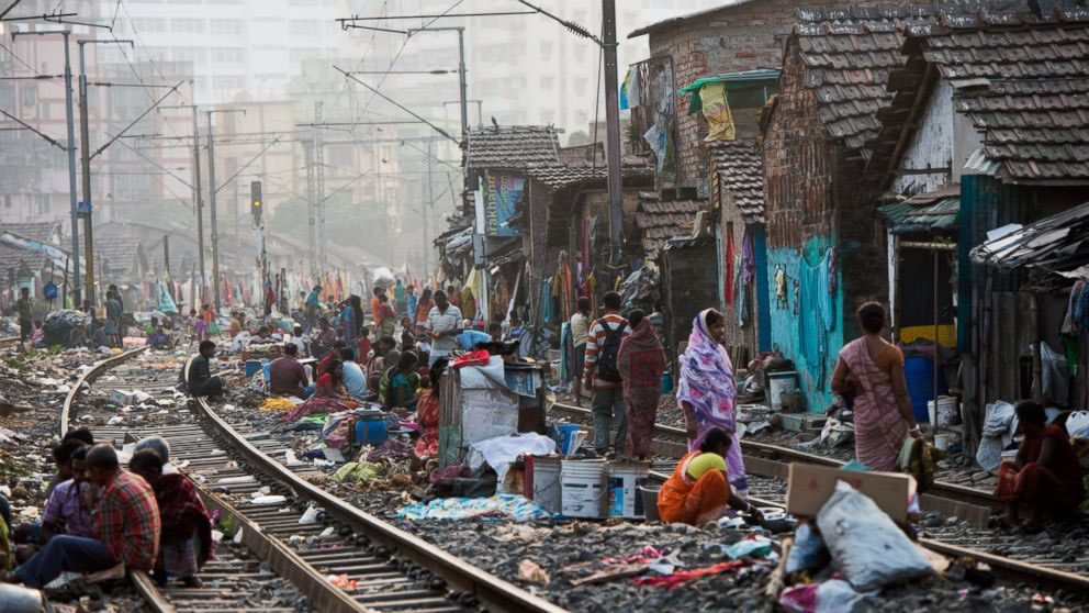 Orang-orang melanjutkan kehidupan mereka di daerah kumuh di rel kereta api saat kereta komuter melintas pada 12 Desember 2013 di Kolkata, India.